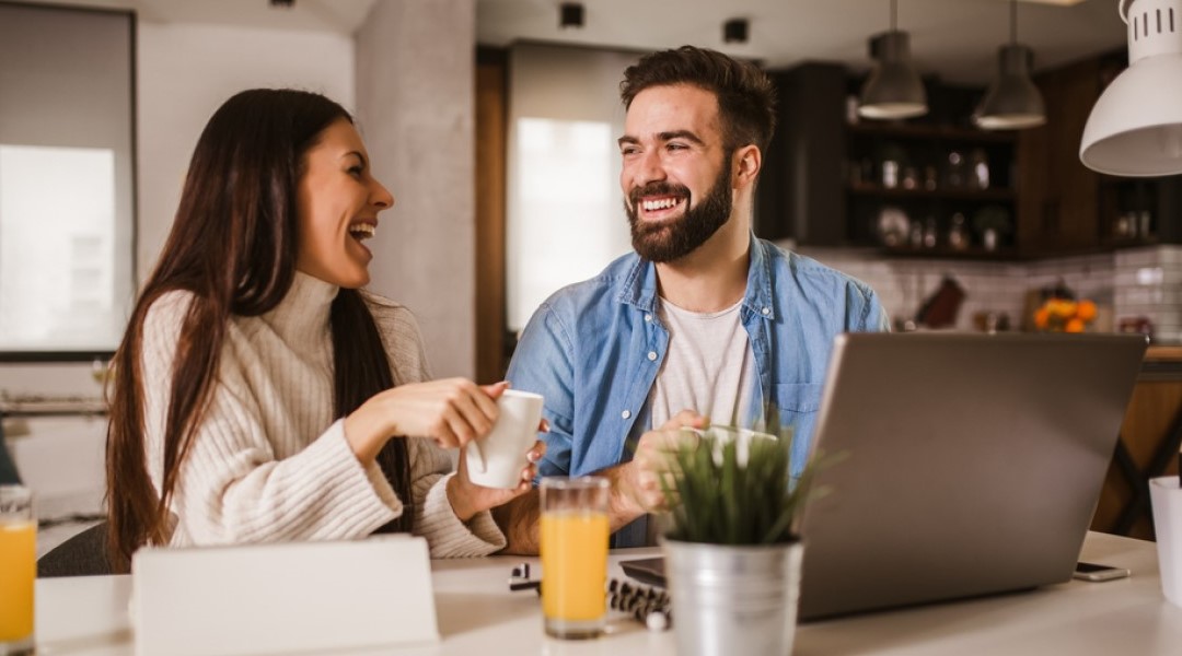 a couple at a bench with their laptop open laughing with each other